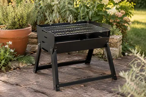 Barbecue portable à charbon Charmline noir déplié sur une surface de jardin, avec sa grille métallique visible.