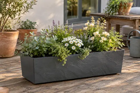 Jardinière rectangulaire anthracite effet pierre, garnie de plantes sur une terrasse en bois