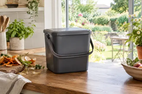 Seau à compost gris de 6 L avec couvercle et anse, posé dans une cuisine près du jardin