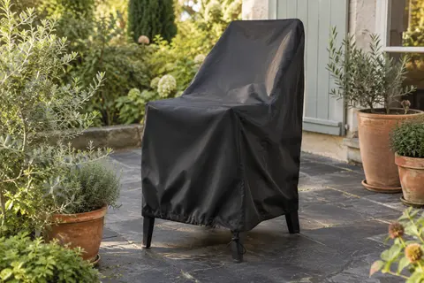 Housse noire en tissu Oxford couvrant une chaise empilable dans un jardin en fin d’été.