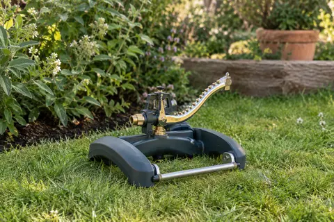 Arroseur-canon Gardena sur traîneau en plastique, avec balancier métallique et gicleurs en laiton dans un jardin