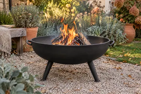 Brasero noir en fonte de 75 cm sur trois pieds, installé dans un jardin aux couleurs d’automne.
