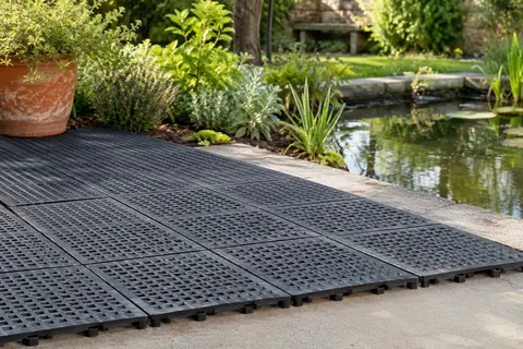 Dalles clipsables noires en PVC ajouré posées sur une terrasse de jardin près d’un bassin