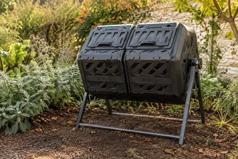Composteur rotatif noir à deux chambres installé dans un jardin d’automne, sur son cadre métallique